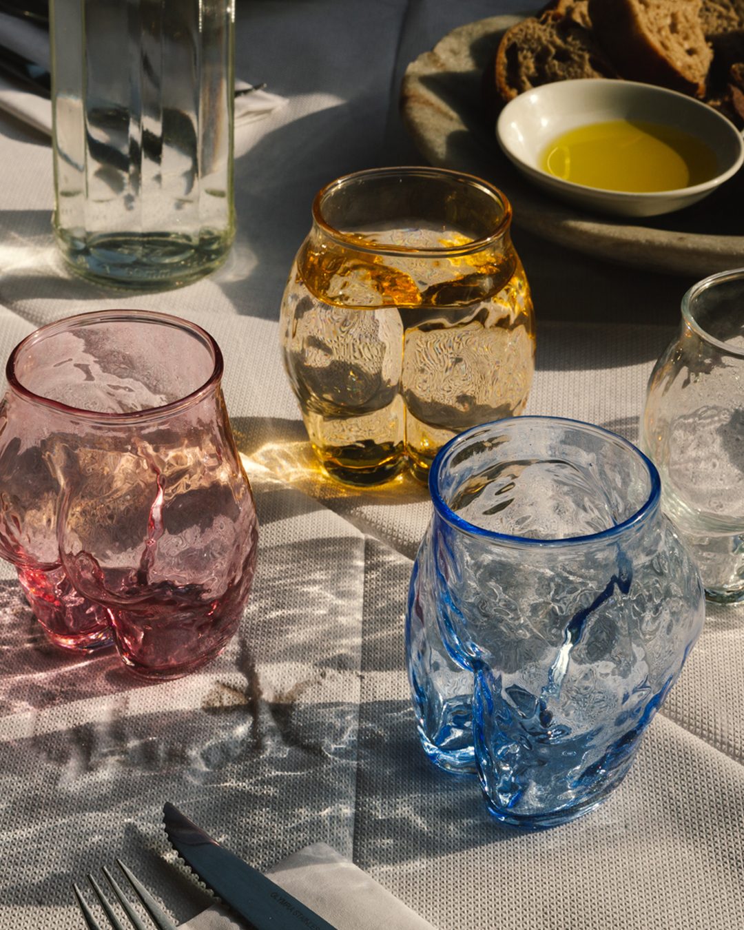 Anissa Kermiche sculpted glasses in pink, amber and blue on a sunlit table